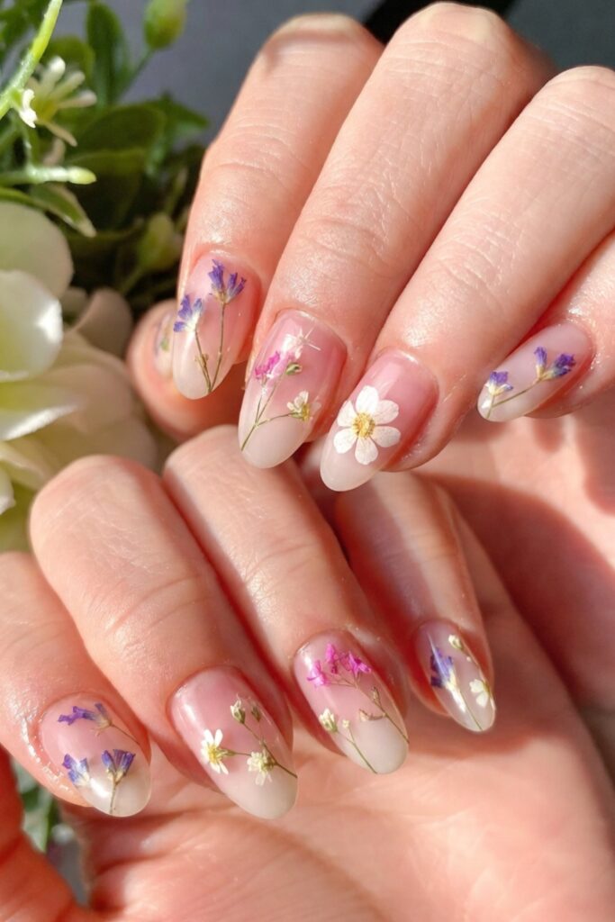 Close-up of dainty pressed flower nails featuring tiny real dried lavender, baby's breath, and miniature daisies sealed in a soft pink and milky white gel base for a delicate, romantic spring manicure.