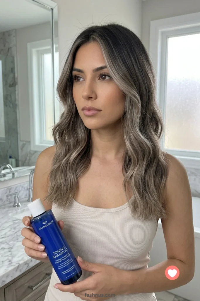 A vertical portrait of a soft, dimensional ash bronde transition, blending cool brunette roots into smoky light ash blonde ends.