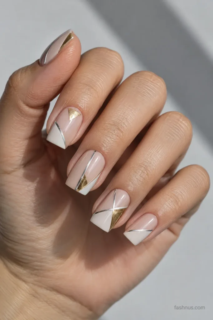 A young Western woman's hand featuring nude-base geometric nail art with precise silver stripes, small gold triangles, diagonal lines, and negative-space details.